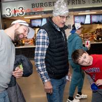 Group of three watching the prize wheel spin at merch table, two with their heads tilted